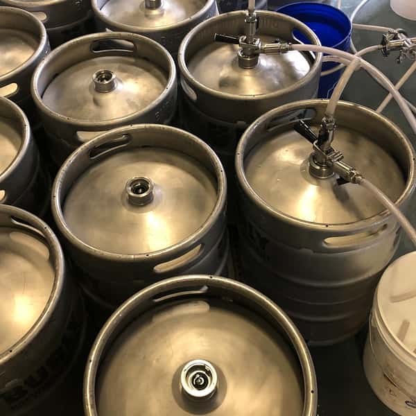 Stainless steel beer kegs being filled and prepared in the brewing process at Alidade Brewing's craft beer production facility.
