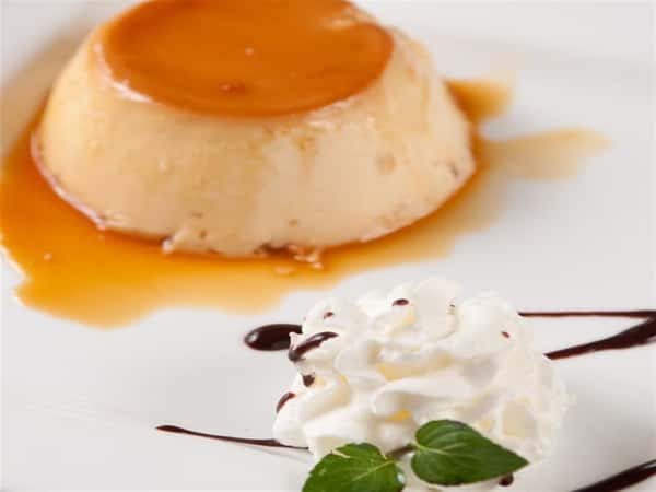 Flan on a white plate with whipped cream, chocolate sauce and mint leaf.