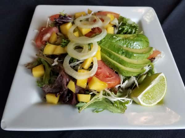 Ensalada de Nelly. Nelly's Salad lettuce, tomatoes, onions, coriander, crushed garlic, apples, flaxseed, avocado (seasonal), olive oil, fresh lime juice.