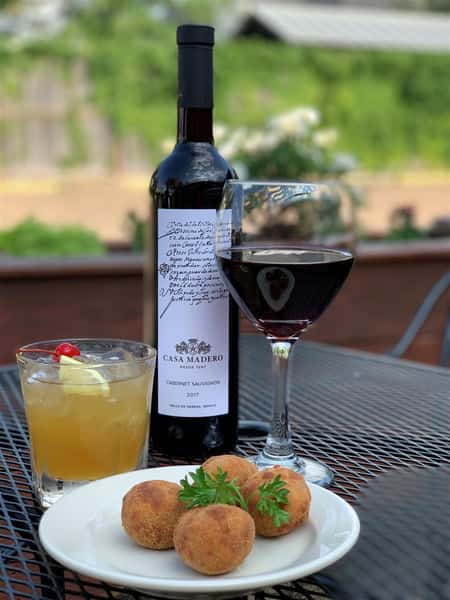 menu item on a table outside with red wine and a cocktail