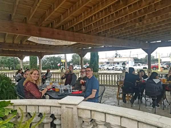 table of five seated in the outside patio enjoying their meal and smiling.