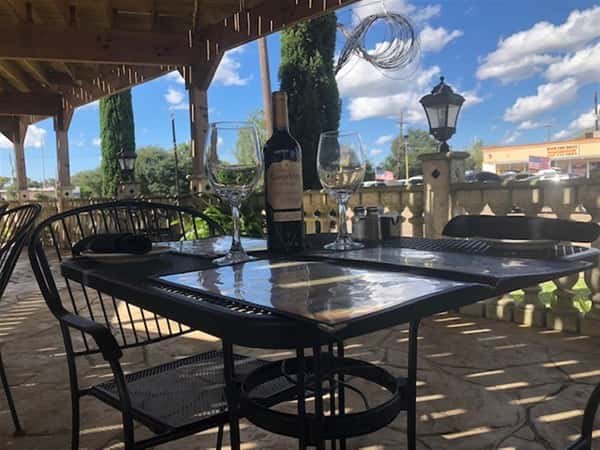 table set in the outside patio with menus, cutlery glassware and a bottle of wine.