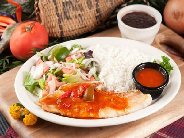 Pargo Criollo. Grilled red snapper filet with Creole sauce on top. Salad and white rice on the side. Plate placed on a wood tray. Tomato, onion and cup of black beans in the background.