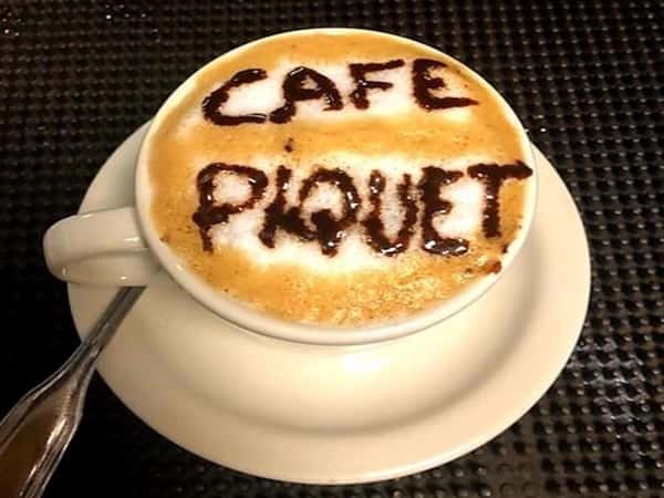 capuccino in a white cup and saucer "cafe piquet" written in chocolate sauce on the foam.