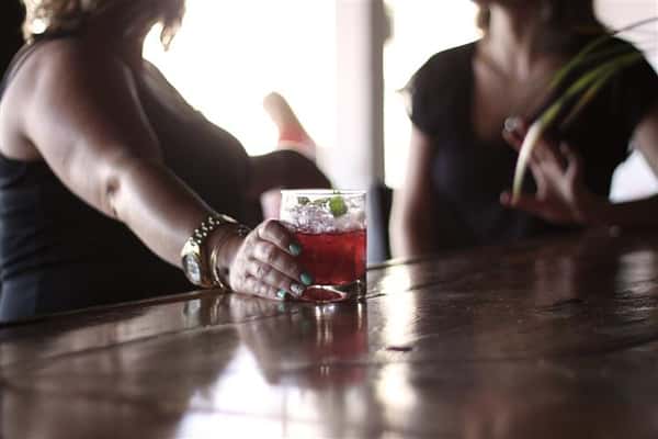 two woman sitting at a bar holding a mixed cocktail