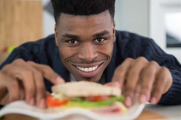 man smiling with half of sandwich in front of him