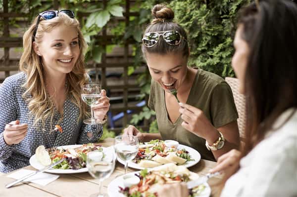 three females sitting at a table smiling and enjoying a meal