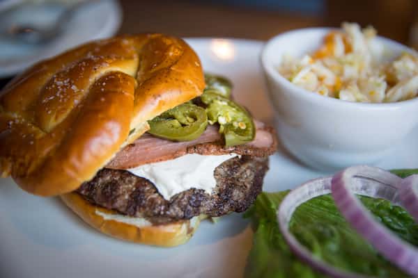 Gourmet burger with grilled beef patty, melted cheese, sliced jalapeños, and bacon on a toasted brioche bun, served with coleslaw at Pourhouse Bar & Grill in Loveland.