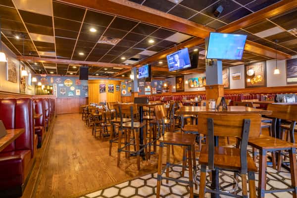 Warm, inviting dining room with wood tables, high-top seating, and multiple TVs creating a lively sports bar atmosphere at Pourhouse Bar & Grill in Loveland.
