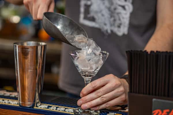 Bartender scooping fresh ice into a martini glass at the bar, highlighting handcrafted cocktails at Pourhouse Bar & Grill in Loveland.