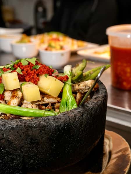 Molcajete bowl with grilled chicken, pineapple, cactus, and chorizo served in a traditional Mexican stone bowl