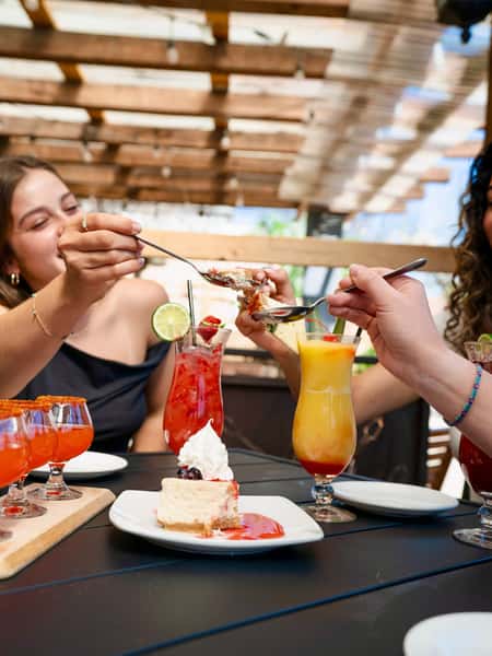 Friends sharing dessert and tropical cocktails on a sunny Mexican restaurant patio during brunch