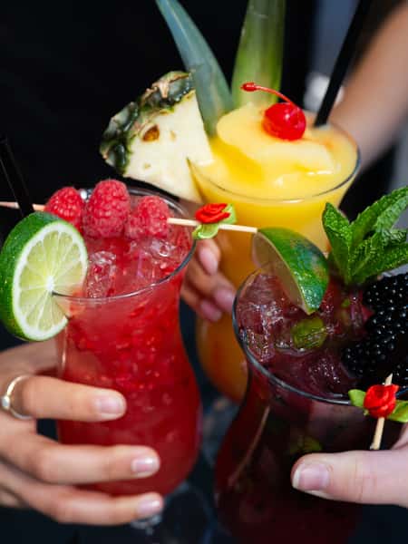 Fresh fruit cocktails with raspberry, pineapple, blackberry, mint, and lime garnishes served at a festive Mexican bar