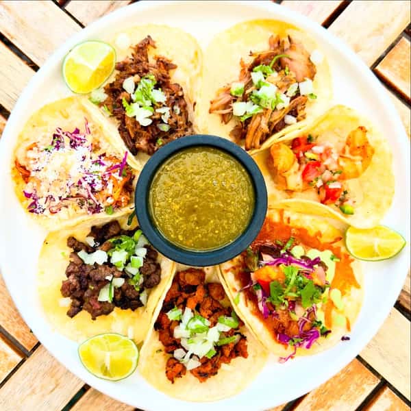 Assorted street tacos with carne asada, shredded pork, shrimp, and fresh salsa served with green salsa and lime wedges