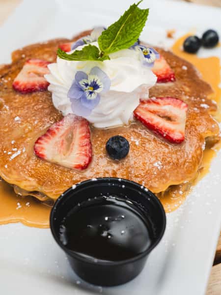 Fluffy pancakes topped with whipped cream, strawberries, blueberries, edible flowers, and maple syrup for Mexican brunch