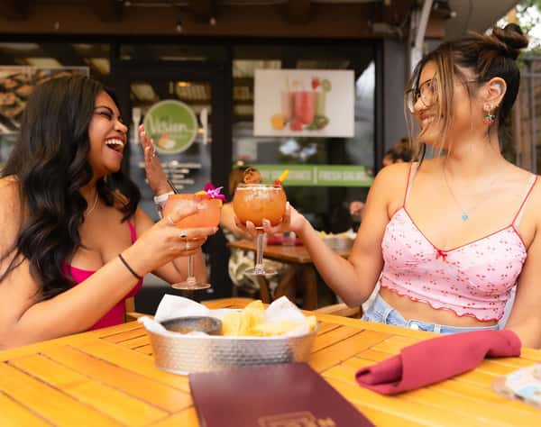 Two friends enjoying margaritas and chips on a sunny outdoor restaurant patio during a fun Mexican brunch date