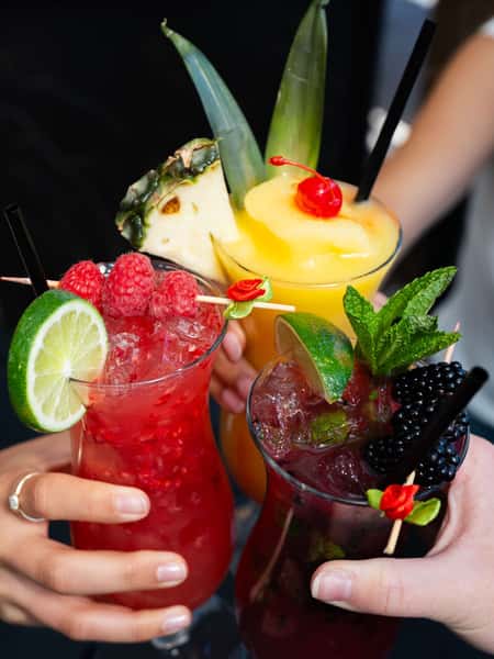 Colorful tropical cocktails with fresh raspberries, blackberries, pineapple, mint, and lime garnishes served at a vibrant Mexican restaurant bar