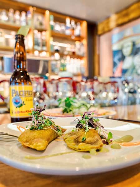 Crispy rolled tacos topped with microgreens and house sauces served with beer at an upscale Mexican restaurant bar