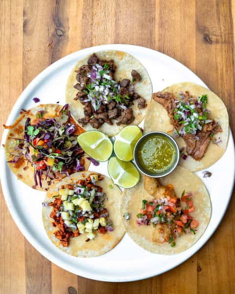 Assorted Mexican street tacos with carne asada, carnitas, shrimp, al pastor, fresh cilantro, onions, lime wedges, and salsa verde