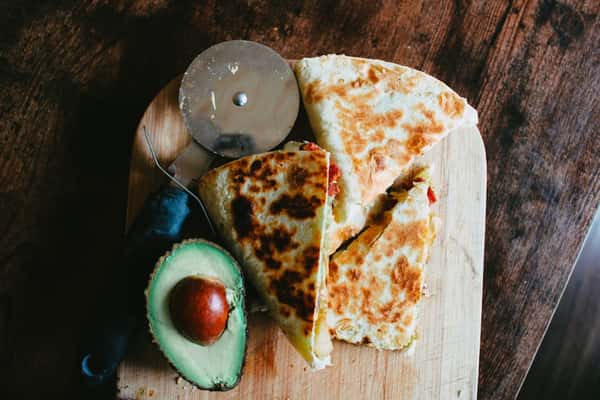 Grilled chicken quesadilla sliced on a wooden board with fresh avocado and pizza cutter, served in a rustic Mexican restaurant setting