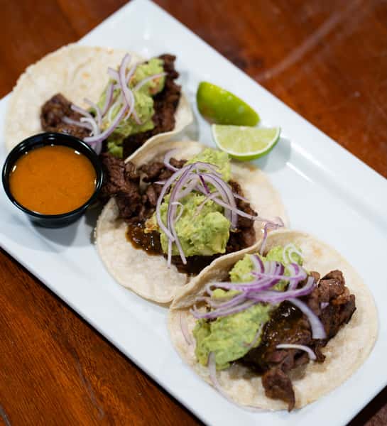 Street tacos with grilled steak, guacamole, red onions, and salsa served with fresh lime wedges
