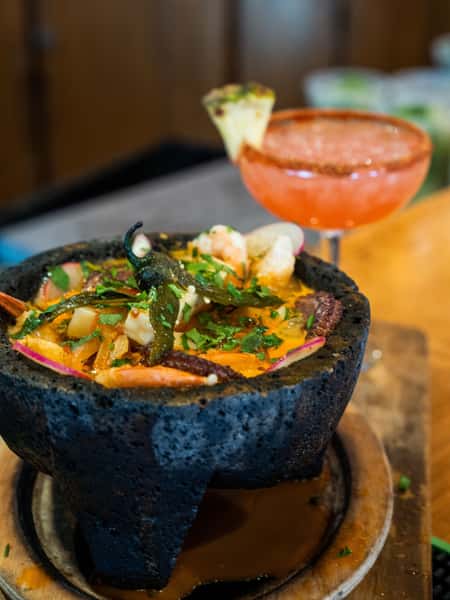 Molcajete seafood and steak dish with grilled cactus, shrimp, and spicy broth served with a fresh margarita