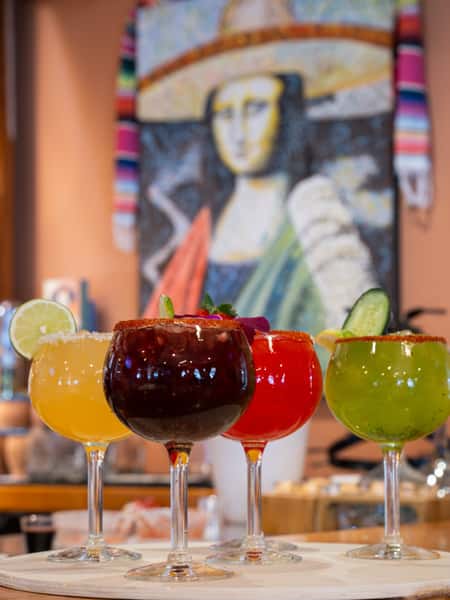 Colorful Mexican cocktails served in oversized goblets with tajin rims inside a vibrant cantina-style restaurant