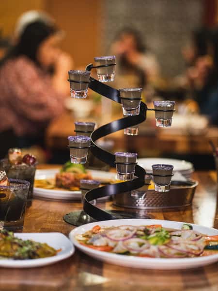 Spiral tequila shot tower with salt-rimmed glasses served over fresh Mexican seafood dishes in a lively restaurant