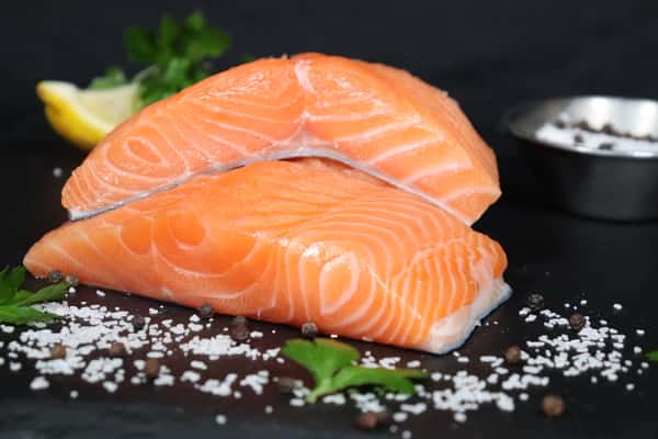 Fresh raw salmon fillets displayed on a bed of ice with coarse salt and herbs.