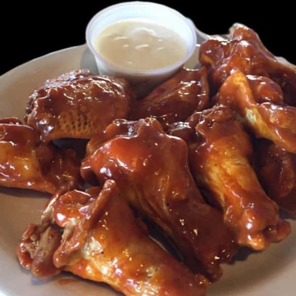 Classic buffalo chicken wings coated in tangy hot sauce, served with a side of creamy ranch dressing on a white plate.
