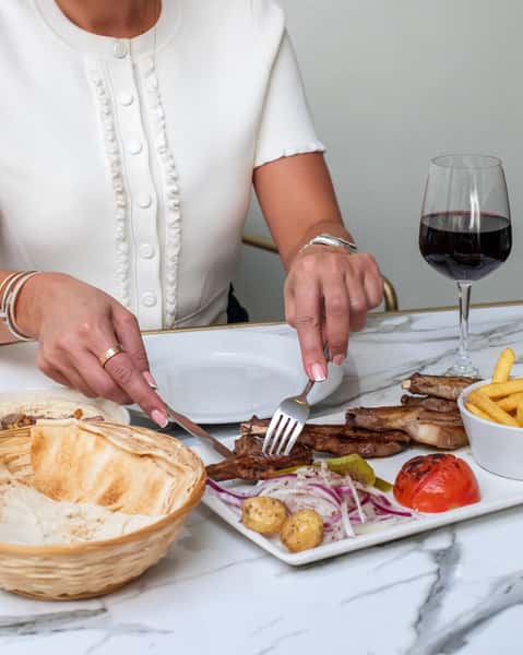 Guest enjoying grilled lamb chops with fries, pita bread, and red wine at a Mediterranean restaurant table