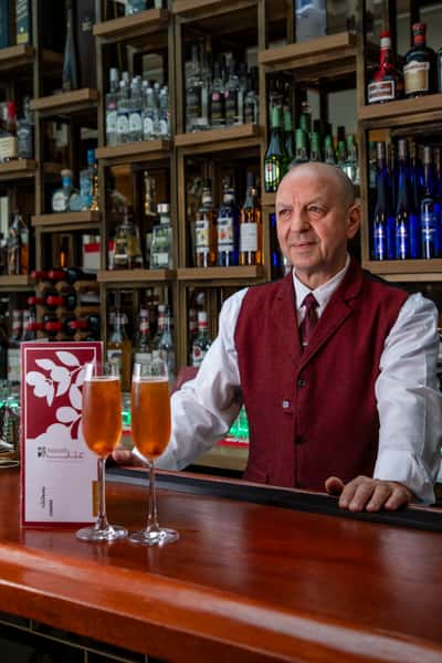 Bartender standing behind a stylish cocktail bar with champagne flutes and premium liquor shelves in an upscale restaurant