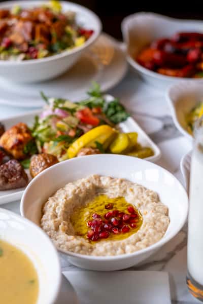 Creamy baba ghanoush topped with olive oil and pomegranate seeds surrounded by fresh Mediterranean mezze and salads