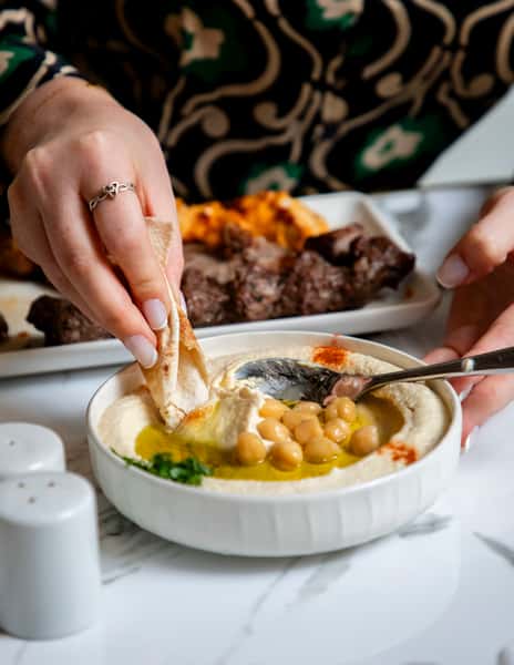 Fresh creamy hummus topped with chickpeas, olive oil, and paprika served with warm pita bread and grilled kebabs