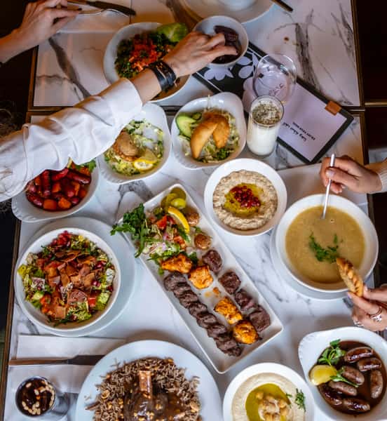 Overhead view of a Mediterranean feast featuring mixed grill kebabs, hummus, lentil soup, fattoush salad, and mezze plates