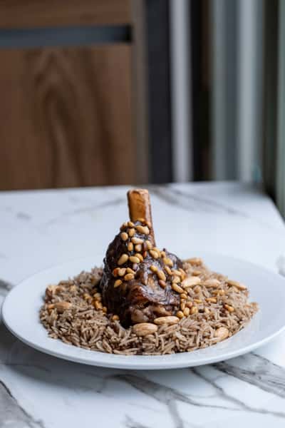 Slow-cooked lamb shank served over seasoned rice with toasted almonds and pine nuts in a modern Mediterranean restaurant