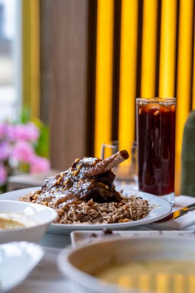 Slow-cooked lamb shank served over fragrant rice with toasted pine nuts and traditional Middle Eastern sides
