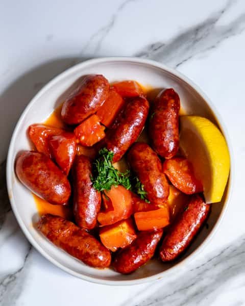 Spicy grilled Mediterranean sausages cooked in rich tomato sauce with fresh parsley and lemon wedge