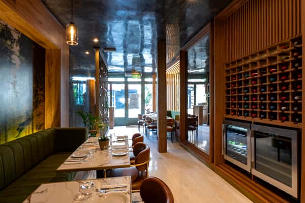 Elegant modern restaurant interior with marble tables, green booth seating, wood accents, and wine display wall