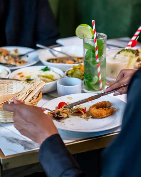 Mediterranean dining table with fresh mezze, pita bread, mojitos, and shared appetizers in a stylish restaurant setting