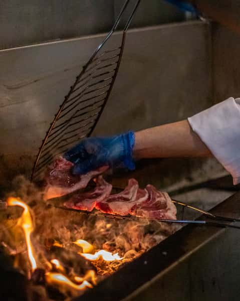 Chef grilling fresh lamb chops over open flames in a smoky restaurant kitchen