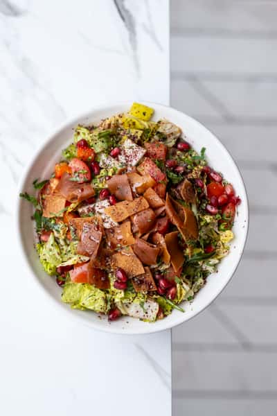 Fresh fattoush salad topped with crispy pita chips, pomegranate seeds, herbs, and diced vegetables