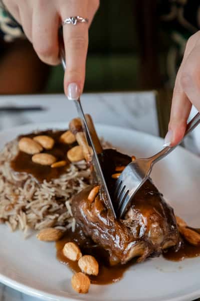 Tender lamb shank carved over fragrant rice with toasted almonds and rich savory sauce at a Middle Eastern restaurant