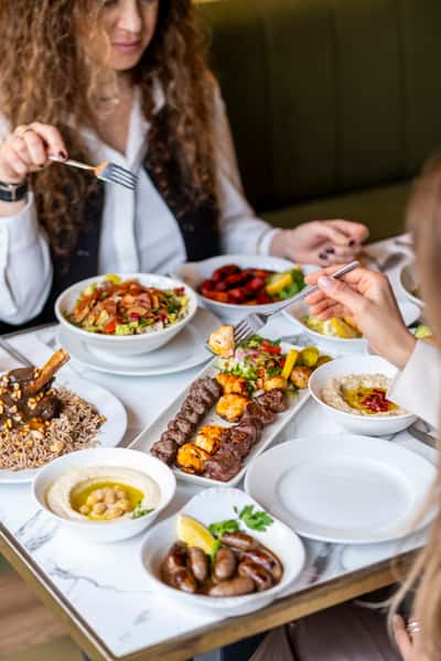 Guests sharing a Mediterranean feast with grilled kebabs, hummus, lamb shank, fattoush salad, and mezze dishes