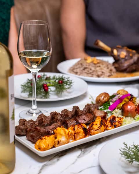 Mixed grilled kebab platter with chicken skewers, beef kebabs, fresh salad, and wine served at an upscale Mediterranean restaurant