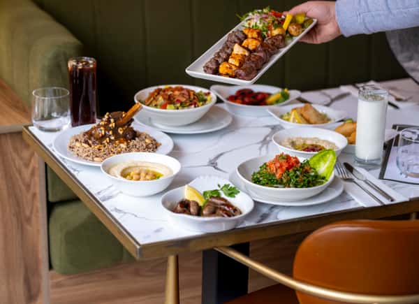 Server presenting a mixed grill platter with kebabs, salad, and Mediterranean appetizers at a restaurant table
