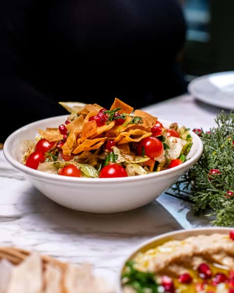 Fresh fattoush salad with crispy pita chips, cherry tomatoes, and pomegranate seeds served on a modern Mediterranean dining table