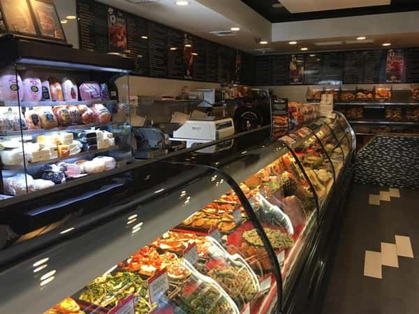 Front counter of store showing a glass with pastries behind it & a sign that says "Form line"