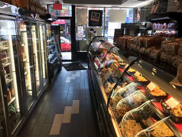 Front of store that shows food behind glass under the counter and refrigerators holding beverages