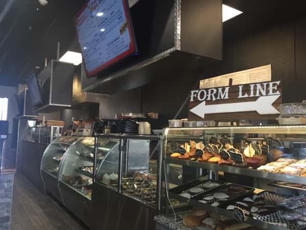 Front counter of store showing a glass with pastries behind it & a sign that says "Form line"